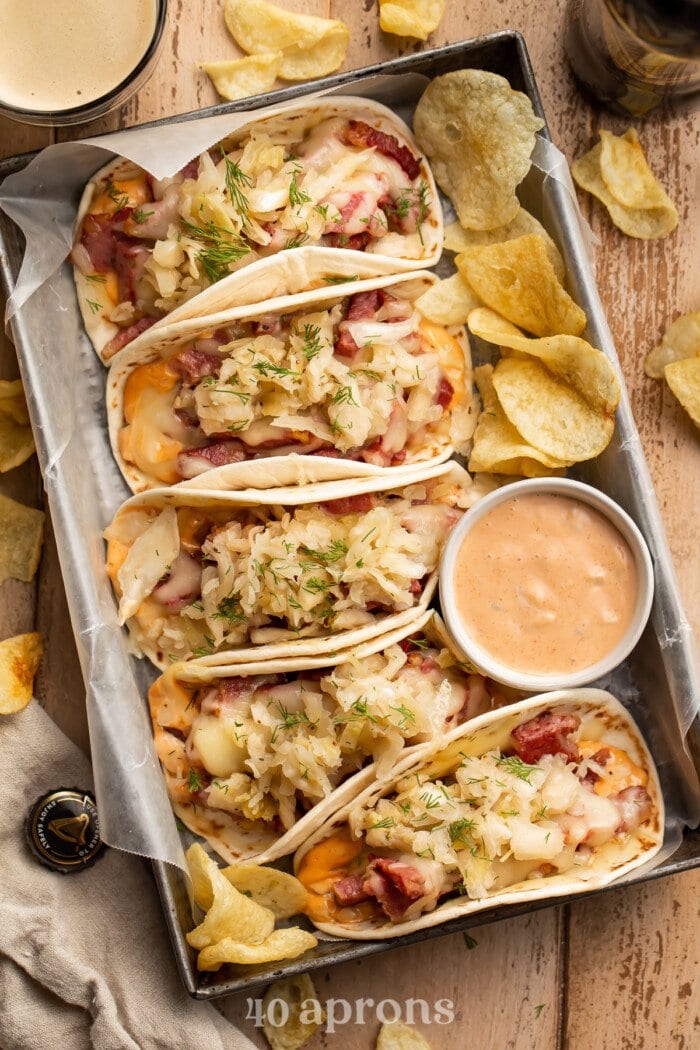 Overhead view of 5 reuben tacos on a serving tray with a bowl of dressing