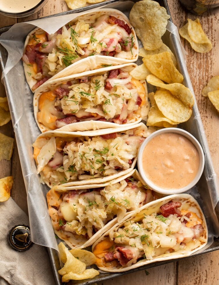 Overhead view of 5 reuben tacos on a serving tray with a bowl of dressing