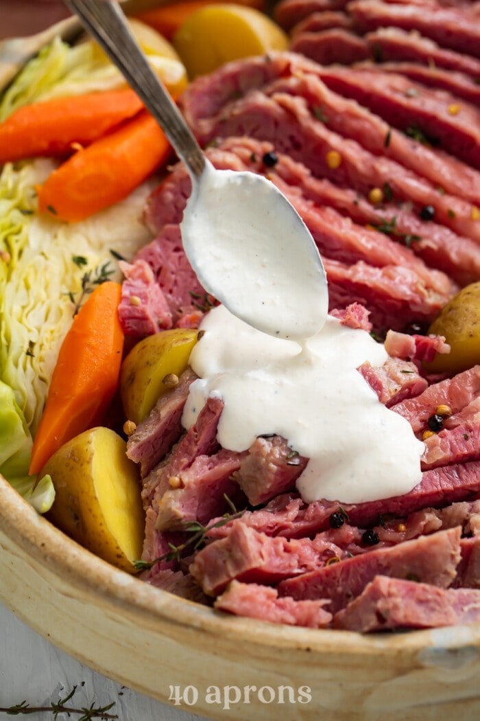 Horseradish spooned over corned beef with potatoes, carrots, and cabbage
