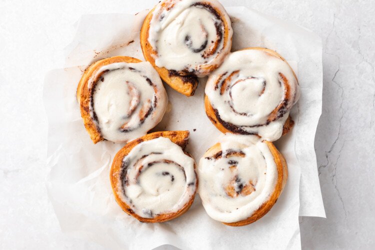 Overhead view of 5 jumbo cinnamon rolls topped with cream cheese frosting on paper towels..