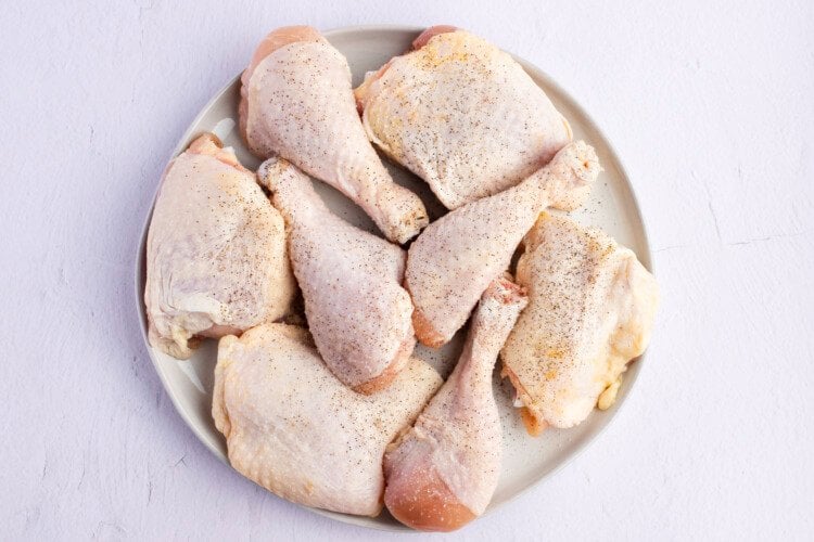 Raw, seasoned chicken thighs and drumsticks on a round plate.