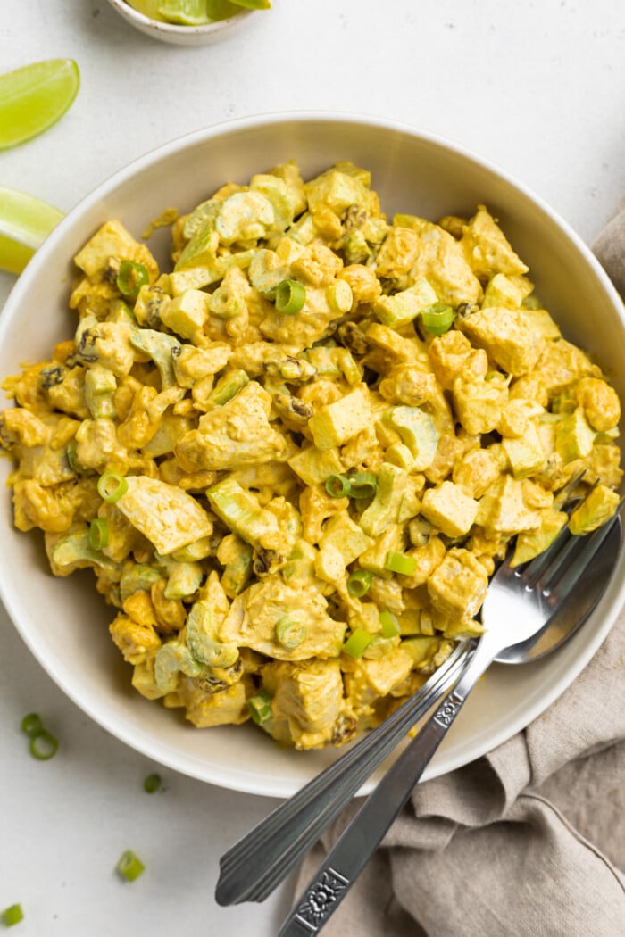 Overhead view of a bowl of curry chicken salad with a spoon on a neutral background.