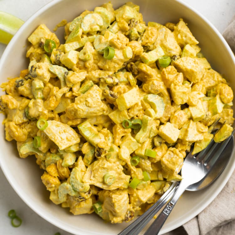 Overhead view of a bowl of curry chicken salad with a spoon on a neutral background.