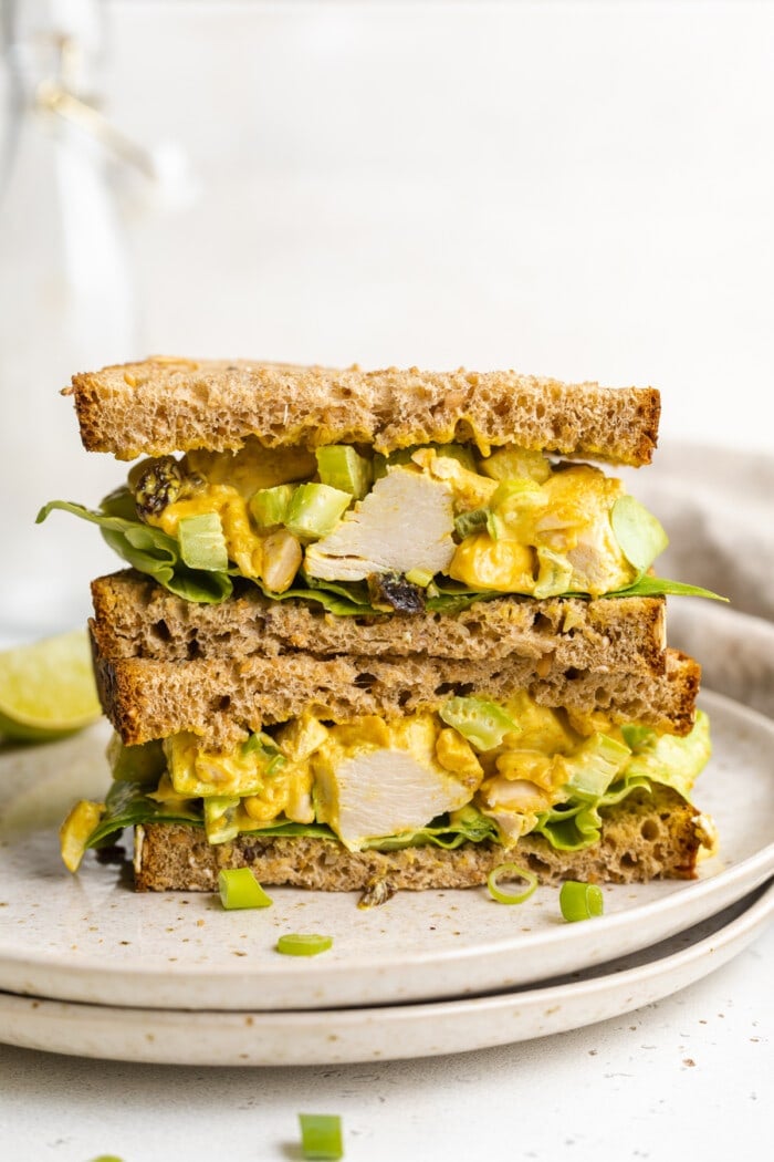 Two halves of a curry chicken salad sandwich stacked on top of each other on a plate.
