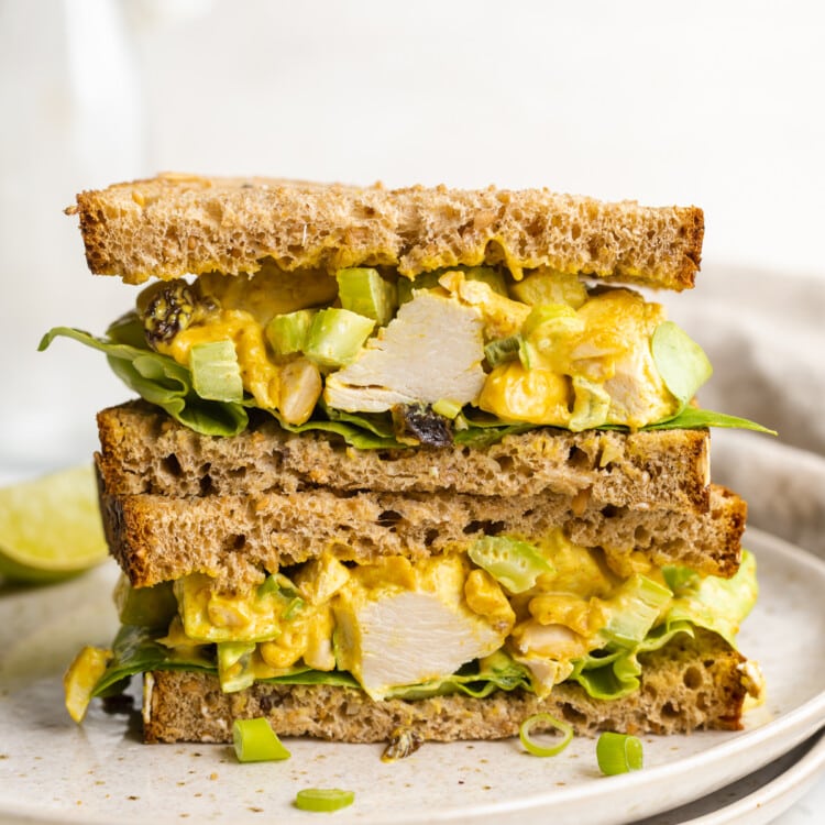 Two halves of a curry chicken salad sandwich stacked on top of each other on a plate.