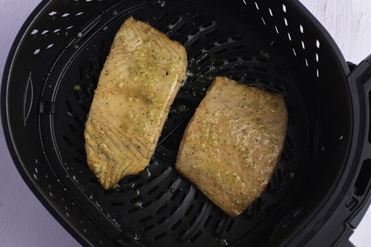 Defrosted salmon fillets in an air fryer basket, brushed with olive oil glaze.