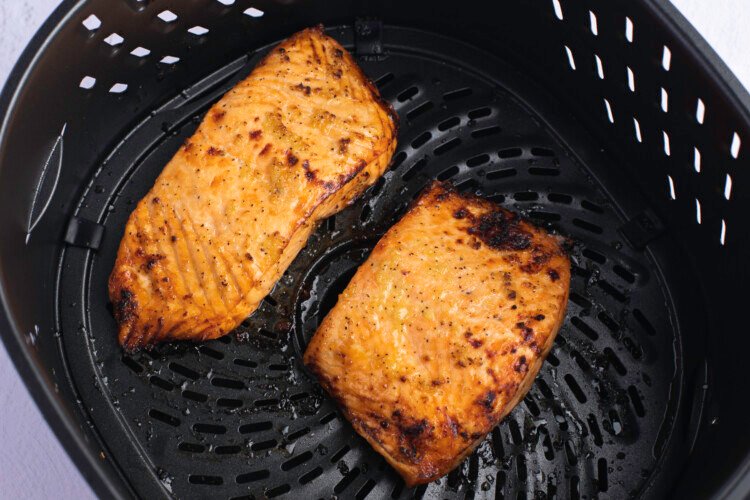 Fully-cooked salmon fillets in a black, round air fryer basket, with dijon mustard olive oil glaze on top.