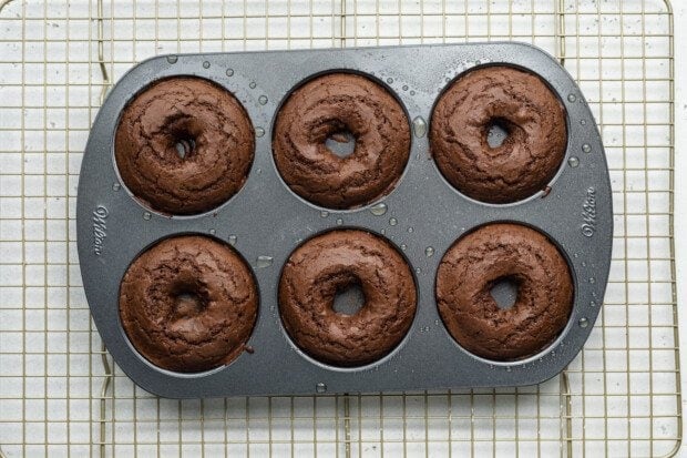 Fully baked chocolate gluten-free donuts in a donut pan on a wire cooling rack.