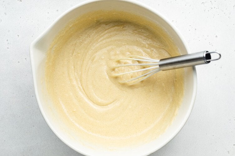 Overhead view of vanilla gluten-free donut batter in large glass mixing bowl with metal whisk.