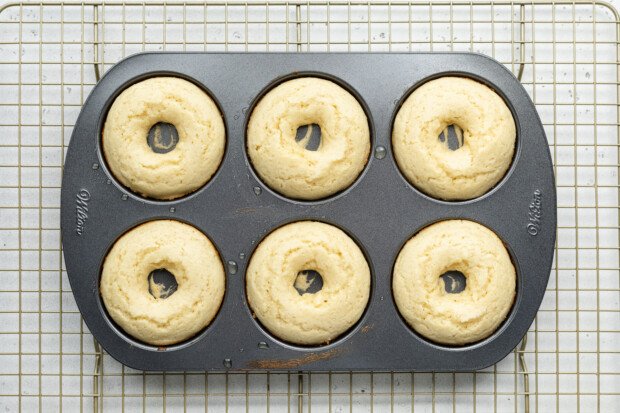 Fully baked vanilla gluten-free donuts in a donut pan on a wire cooling rack.