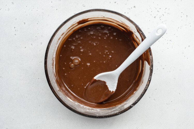 Overhead view of chocolate icing for chocolate gluten-free donuts in a large glass mixing bowl with a spoon.