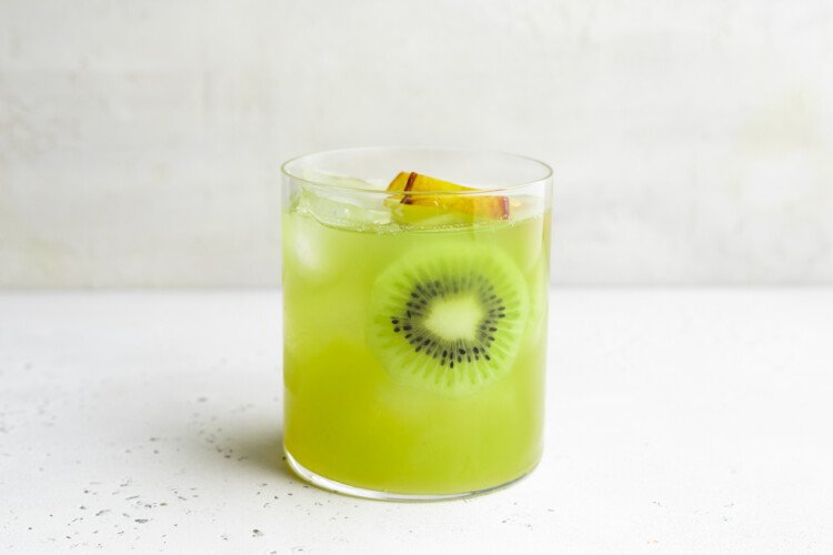 Side view of a single glass containing kiwi starfruit refresher, ice, and slices of starfruit and kiwi.