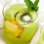 Close-up, 3/4 angle view of a glass of lime green kiwi starfruit refresher with slices of kiwi and starfruit.