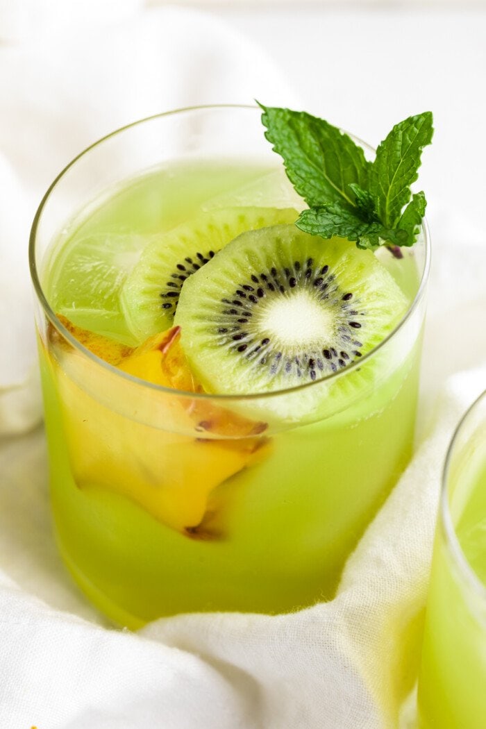 Close-up, 3/4 angle view of a glass of lime green kiwi starfruit refresher with slices of kiwi and starfruit.