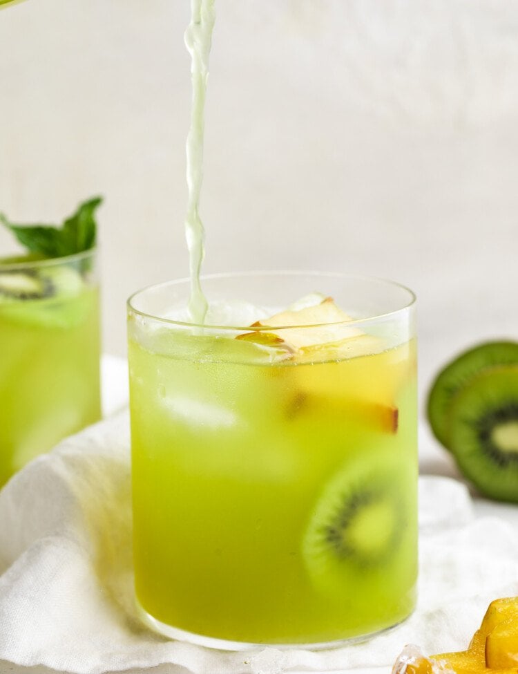 Lime green kiwi starfruit refresher poured into a glass with ice and slices of starfruit and kiwi.
