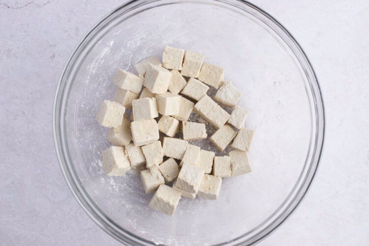 Cornstarch-coated tofu cubes in large glass mixing bowl on white background.