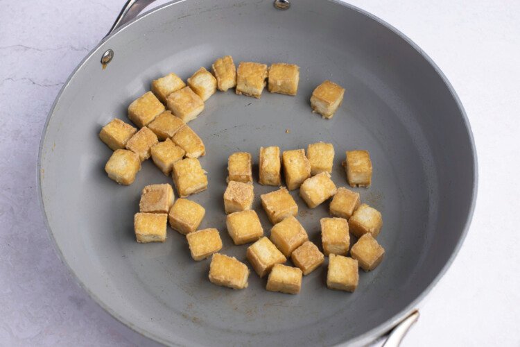 Cooked tofu cubes in large grey skillet on white background.