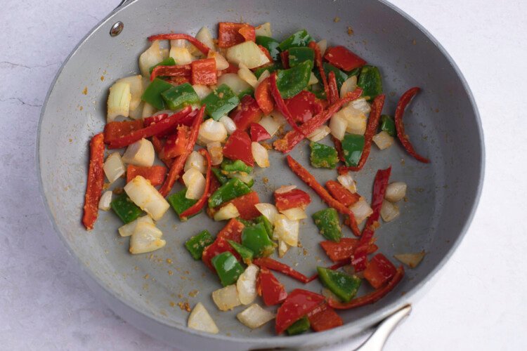 Red chilis, red bell peppers, green bell peppers, white onion, and ginger in large skillet.