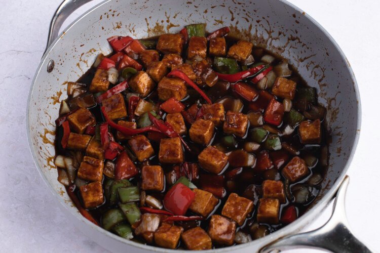 Kung Pao tofu with sauce and veggies in a large grey skillet against a white background.