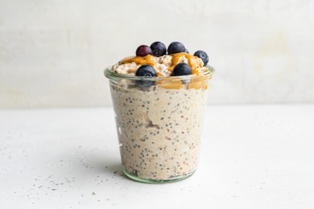 Side view of a jar of peanut butter overnight oats topped with peanut butter and blueberries.