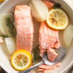 Overhead view of poached salmon with lemon and onion in a bowl.