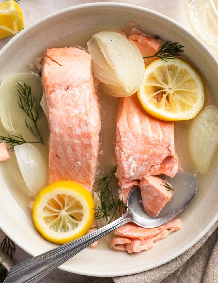 Overhead view of poached salmon with lemon and onion in a bowl.