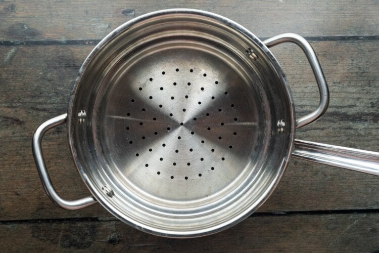 Steamer basket insert in large saucepan on wooden tabletop, shown from directly overhead.