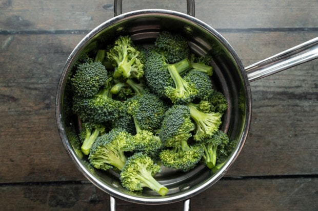 Broccoli florets in steamer basket insert in large saucepan on wooden table.