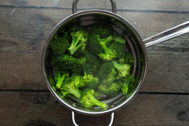 Bright green steamed broccoli florets in steamer basket inserted into large saucepan.