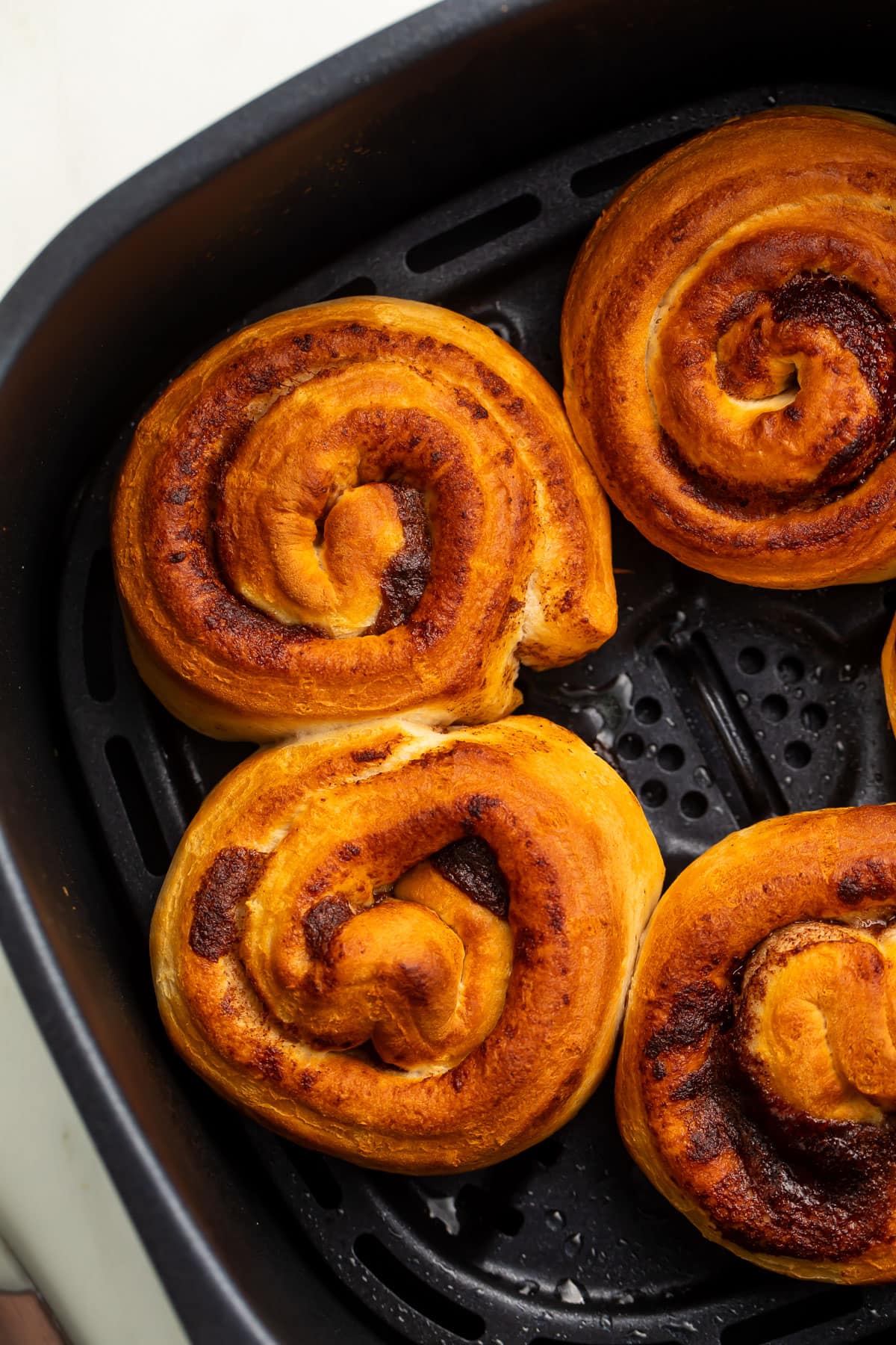 Cinnamon rolls in an air fryer basket, without icing on top, showing the swirl of the cinnamon.