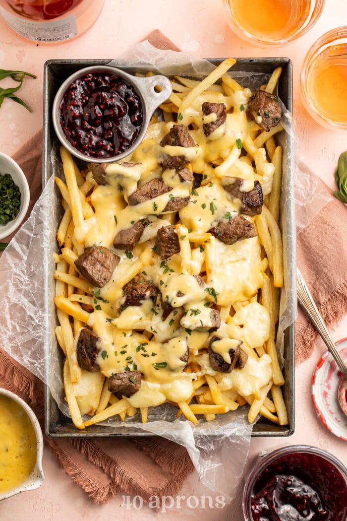Overhead view of baked brie and steak cheese fries in a rectangular deep pan with raspberry preserves.