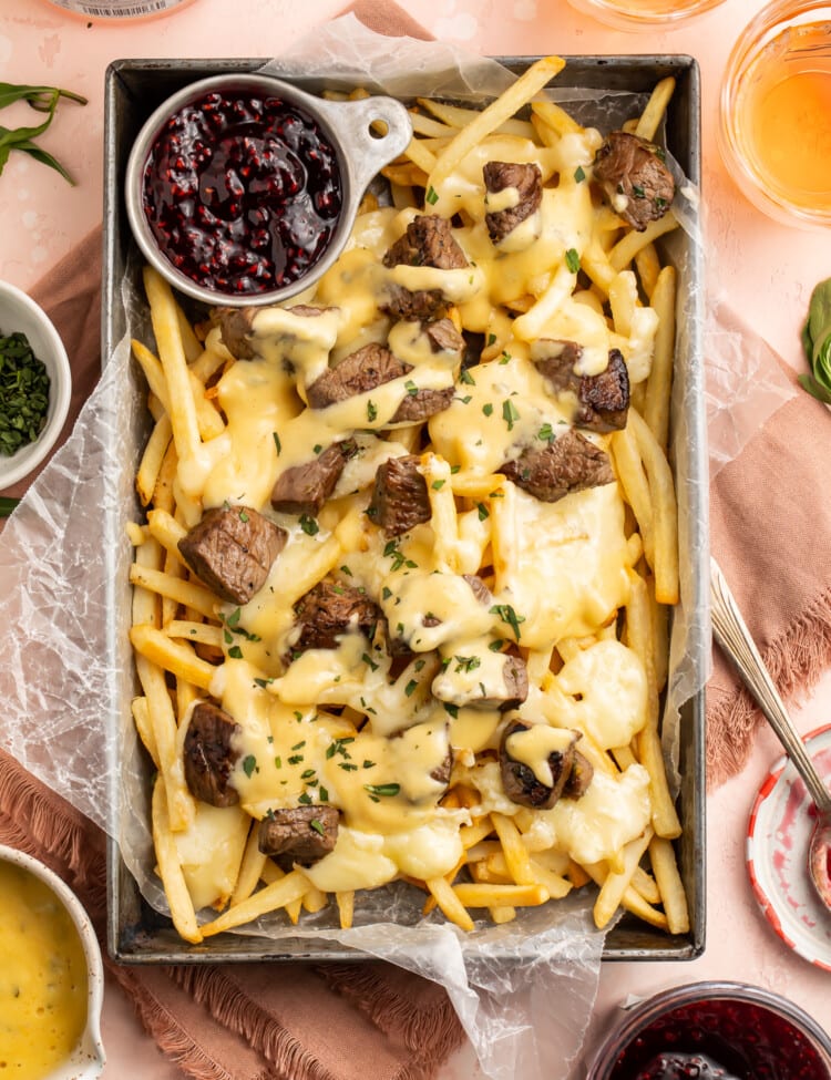 Overhead view of baked brie and steak cheese fries in a rectangular deep pan with raspberry preserves.