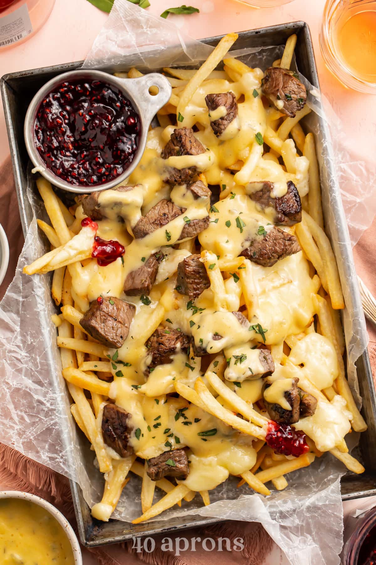 Overhead, angled view of baked brie and steak cheese fries in a rectangular deep pan with raspberry preserves.