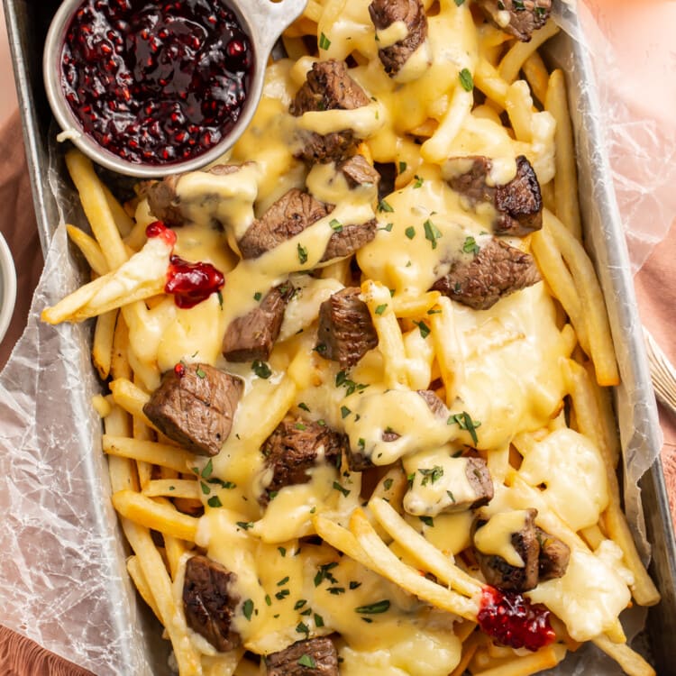 Overhead, angled view of baked brie and steak cheese fries in a rectangular deep pan with raspberry preserves.