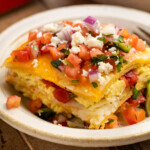A square slice of breakfast taco casserole on a white plate, showing the layers of tortilla, eggs, and pico.