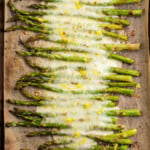 Overhead view of a row of roasted asparagus on a baking sheet, covered in melted cheese.