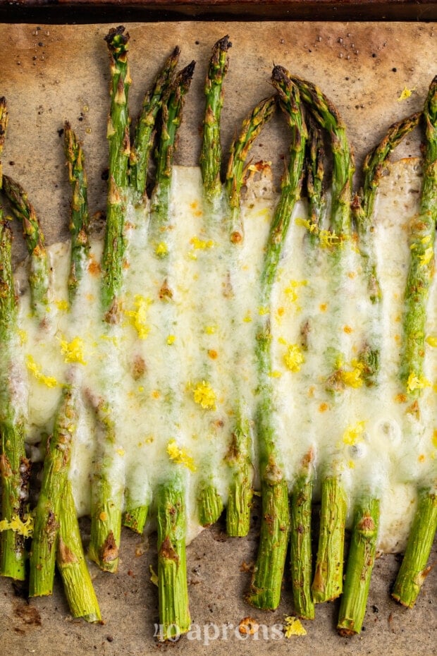 Overhead view of roasted asparagus spears covered in cheese on a baking sheet lined with parchment paper.