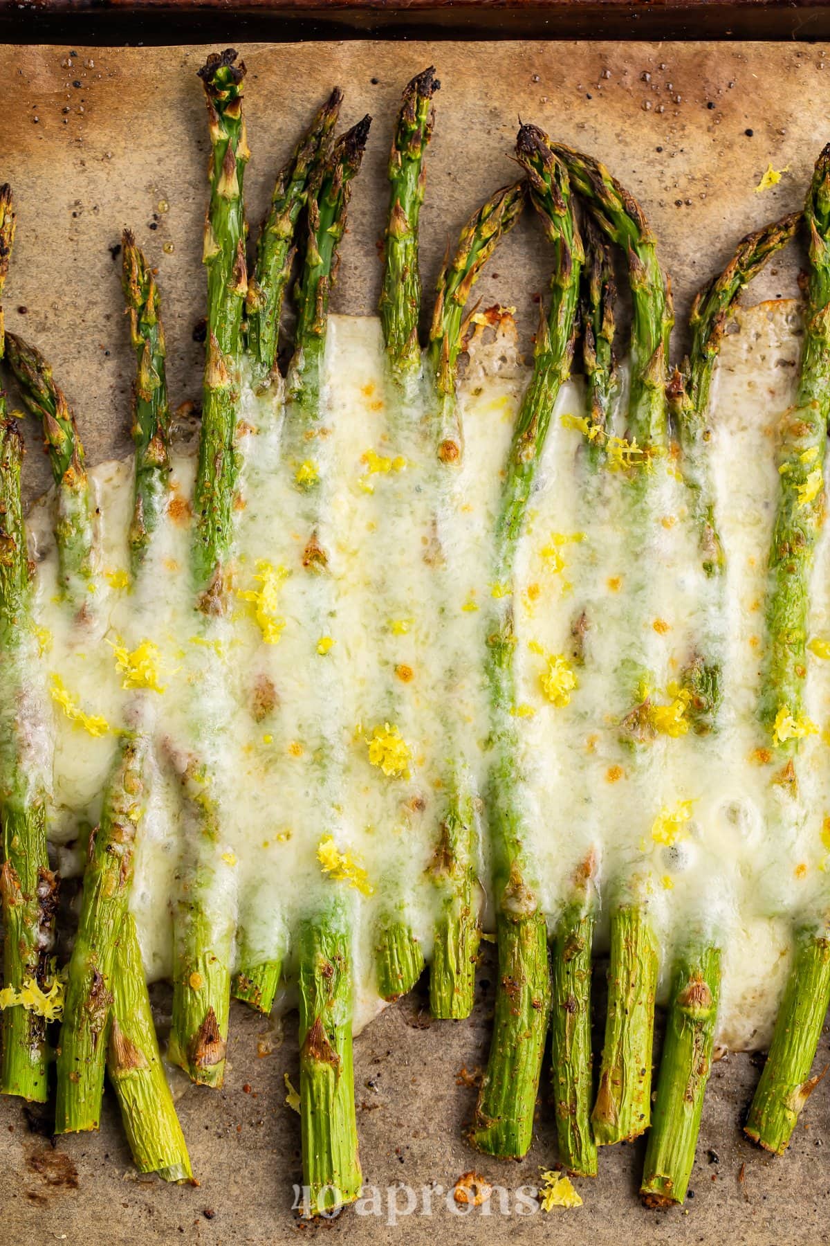 Overhead view of roasted asparagus spears covered in cheese on a baking sheet lined with parchment paper.