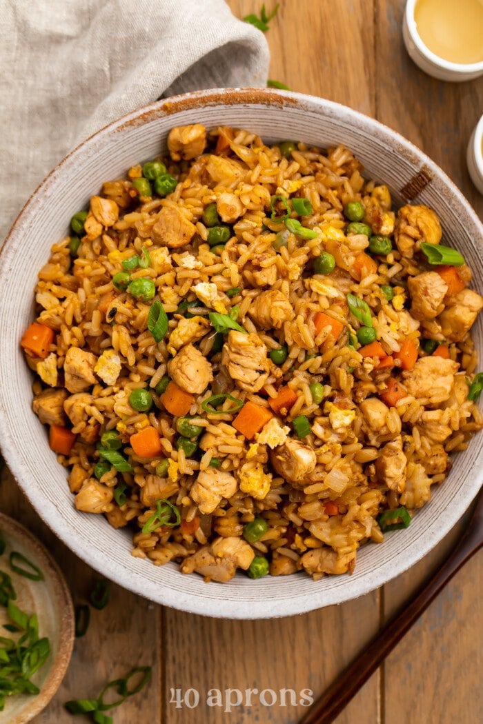 Overhead view of a bowl of chicken fried rice on a wooden table.