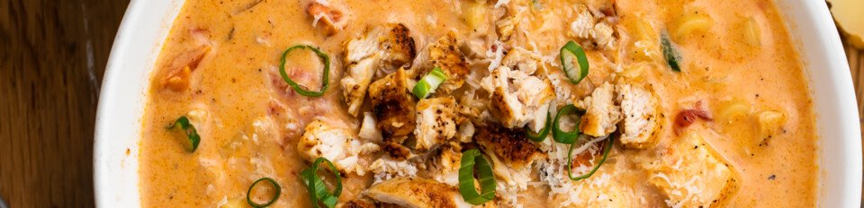Overhead view of one bowl and one partial bowl of cajun chicken pasta soup on a wooden table.