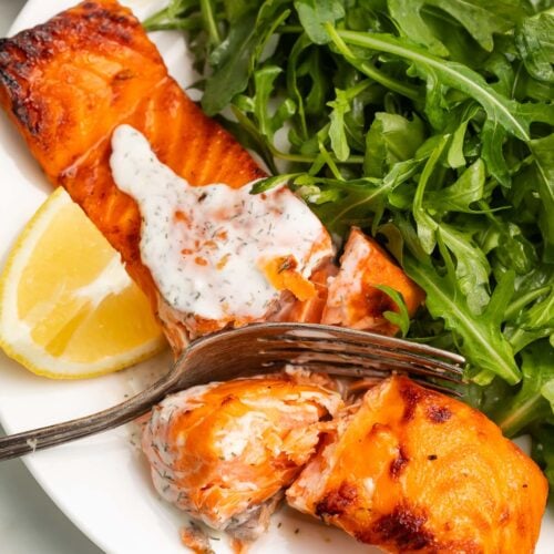 A salmon fillet, cooked in an air fryer, topped with a creamy dill sauce and served with a small salad.