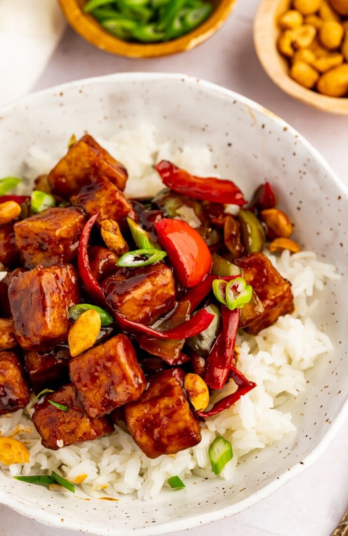 Overhead view of kung pao tofu and stir-fried veggies in a bowl with white rice and green onions.