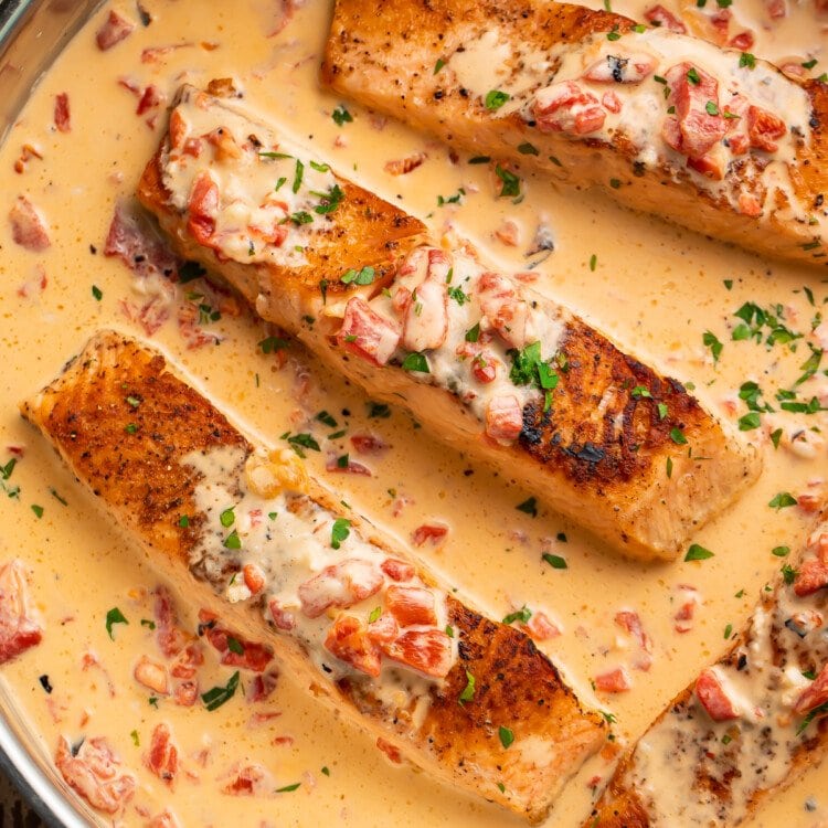 Overhead view of 4 salmon fillets in a large silver saucepan with red pepper parmesan sauce.