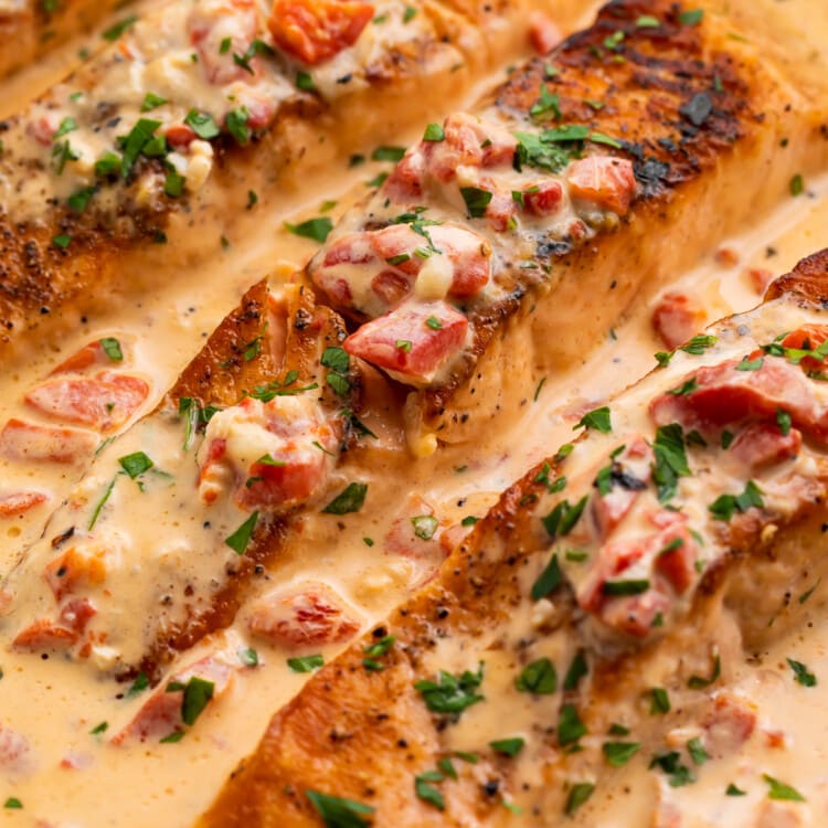 Overhead close-up of 3 salmon fillets in a silver saucepan with a creamy sauce.