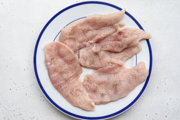 4 chicken cutlets seasoned with salt and black pepper on a round white plate with blue trim.