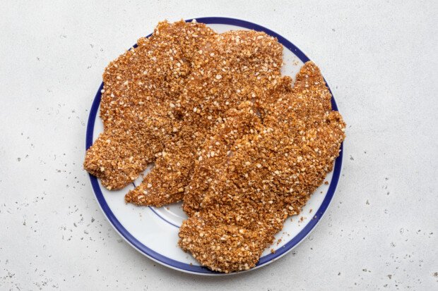 Overhead view of uncooked pecan-crusted chicken on a white plate with blue trim.