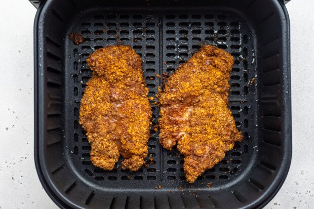 Overhead view of 2 cooked pecan-crusted chicken cutlets in the air fryer basket.