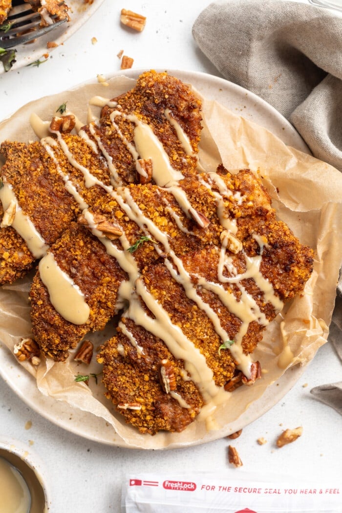 Top view of a plate of 3 pecan crusted chicken cutlets with a drizzle of honey mustard sauce on a neutral plate.