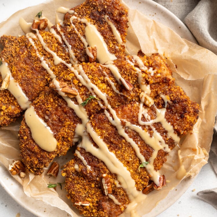 Top view of a plate of 3 pecan crusted chicken cutlets with a drizzle of honey mustard sauce on a neutral plate.