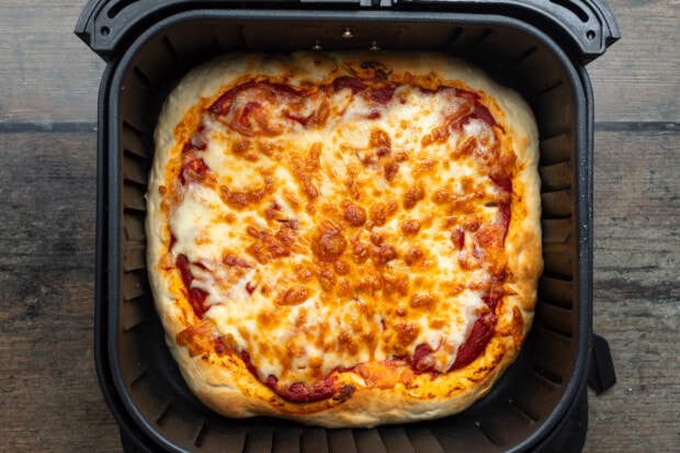 Overhead view of a fully baked air fryer pizza topped with pizza sauce and shredded cheese in an air fryer.